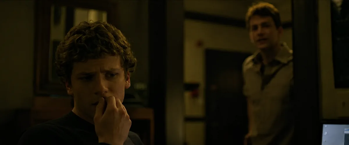 The same scene reimagined: Zuckerberg, worried, biting his fingers at the monitor while Eduardo stands in the doorway